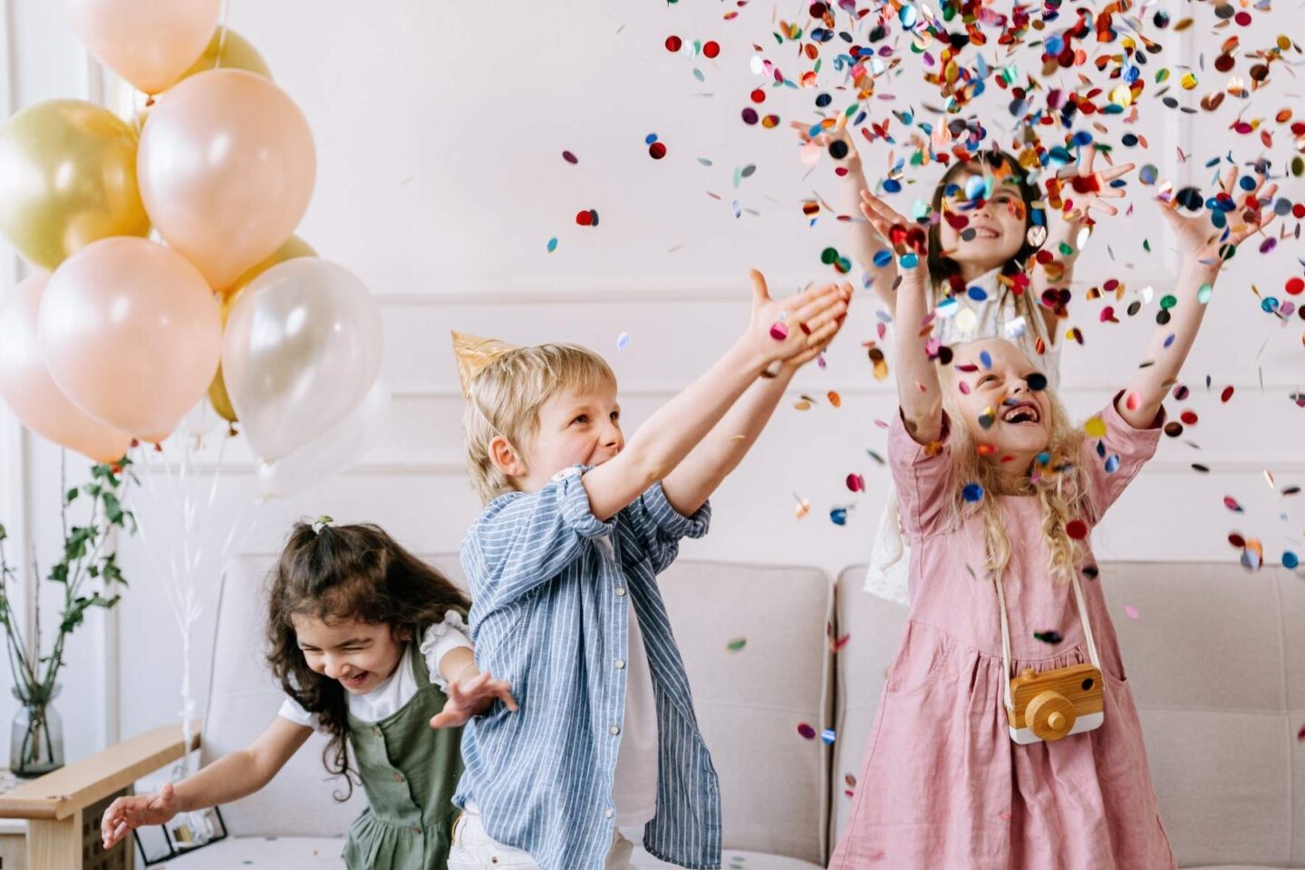 Kinder mit bunten Partyhüten auf dem Kopf werfen Konfetti in die Luft und lachen.