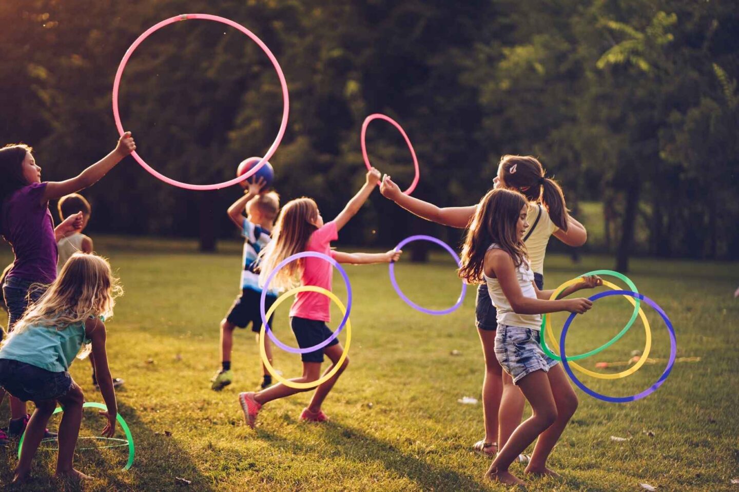 Kinder rennen fröhlich über eine Wiese und spielen mit bunten Ringen in unterschiedlichen Größen. 
