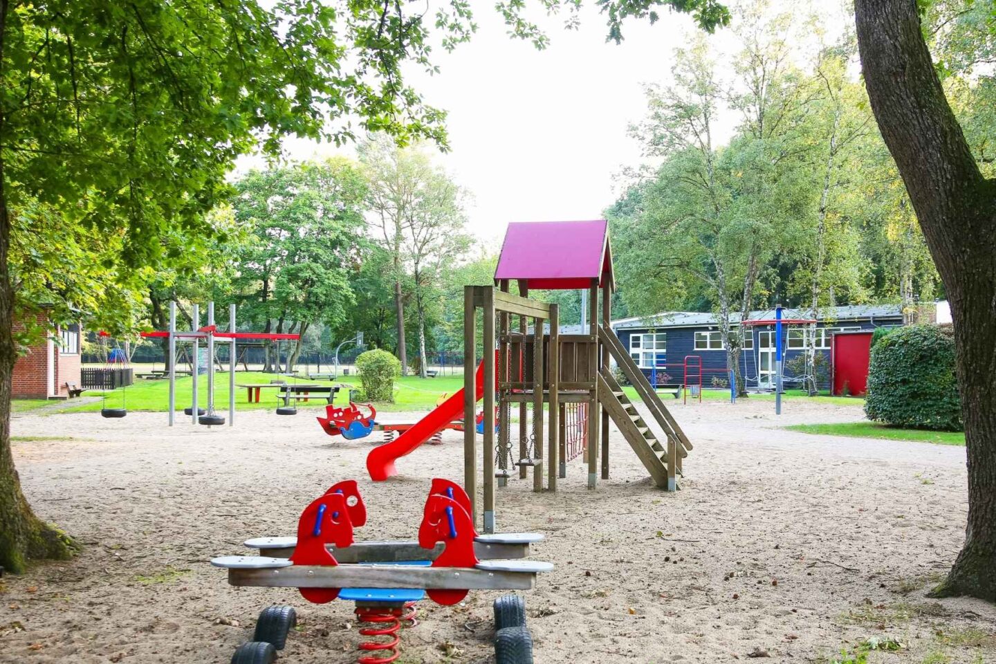 Großes Außengelände der Freiluftschule Fischbeker Heide mit Klettergerüst, Rutsche, Schaukel, Wipp-Tieren, Tischtennisplatte und viel Grünfläche.