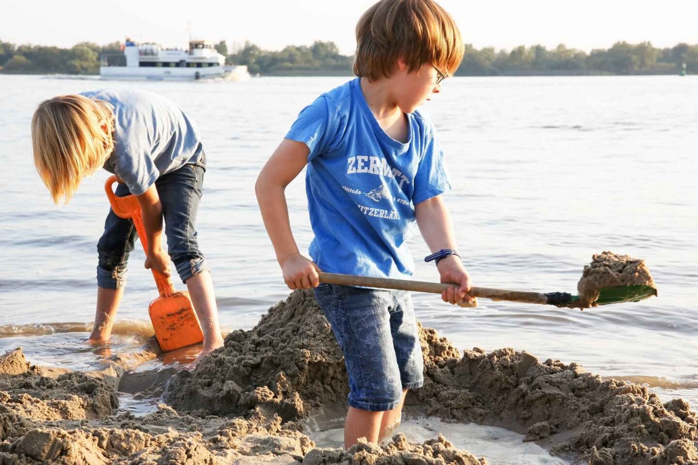 Zwei Kinder die am Elbstrand im Wasser stehen und mit Schaufeln im Sand buddeln.