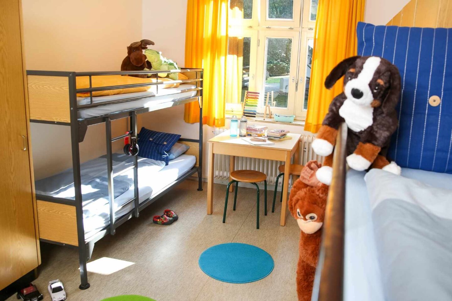 Helles Mehrbettzimmer der Freiluftschule Wittenbergen mit Spielzeug und Kuscheltieren.