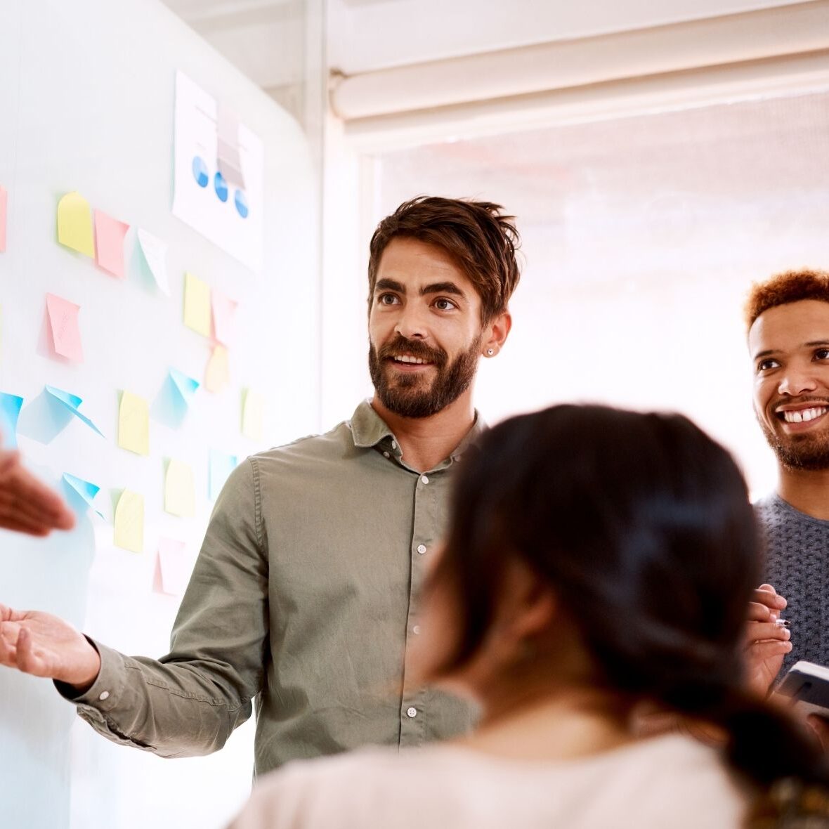 Eine Gruppe von Personen steht vor einem Whiteboard miut Post-Its drauf.