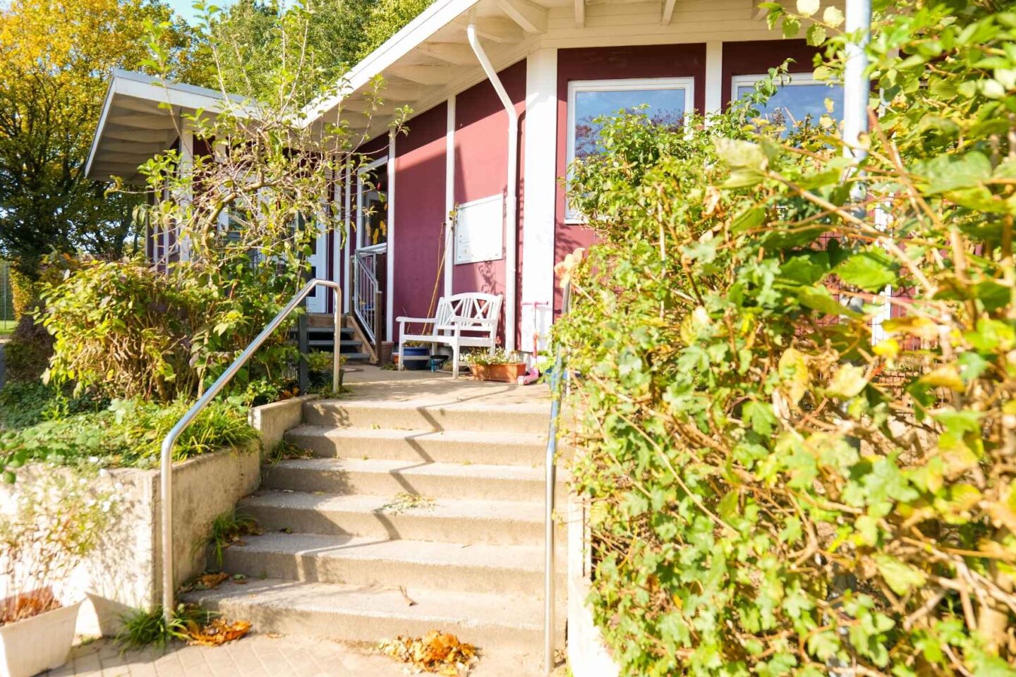 Treppenaufgang und Eingang der Kita Eckerkoppel, umgeben von grünem Garten und herbstlicher Natur.