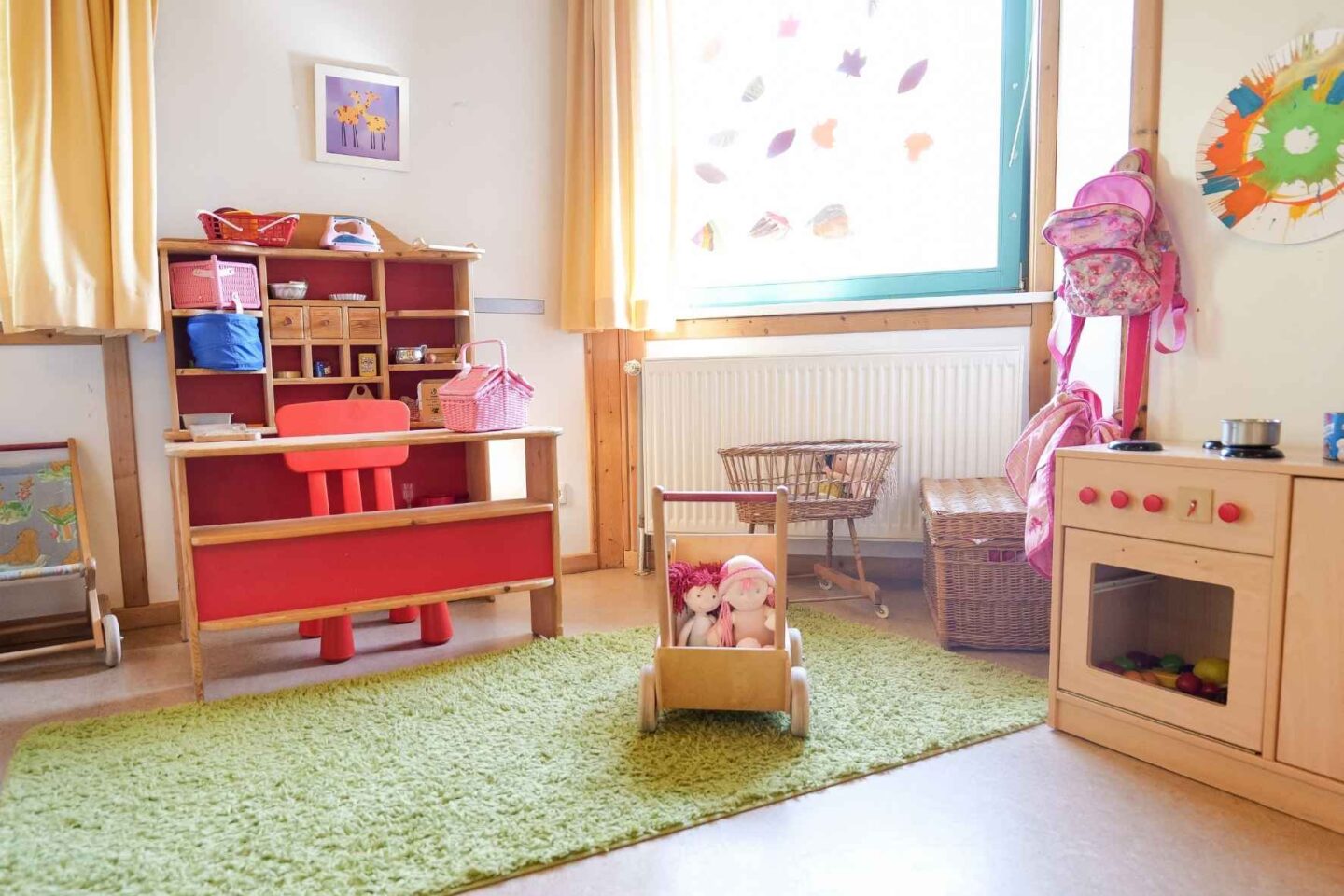 Puppenecke im Gruppenraum der Kita Eckerkoppel mit Holzspielküche, Puppenwagen und farbenfrohen Spielmaterialien.