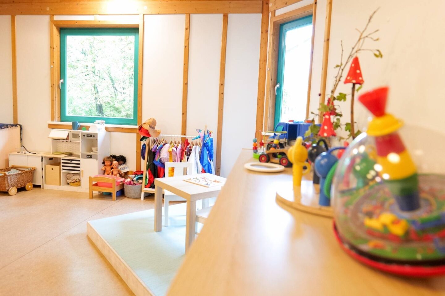 Heller Gruppenraum in der Kita Osterbrook mit bunten Wänden, großen Fenstern, einer Verkleidungsstange und einer Spielküche.