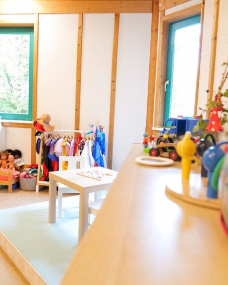 Heller Gruppenraum in der Kita Osterbrook mit bunten Wänden, großen Fenstern, einer Verkleidungsstange und einer Spielküche.