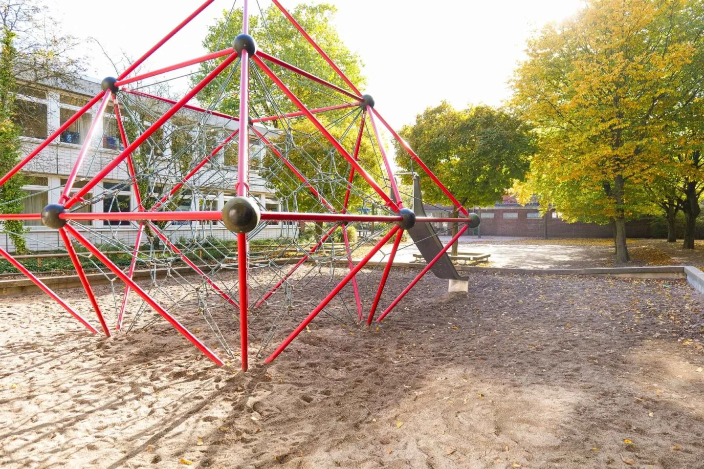 Rotes Klettergerüst in Würfelform mit Rutsche in einem Sandkasten auf dem grünen Außengelände der Kita Redder.
