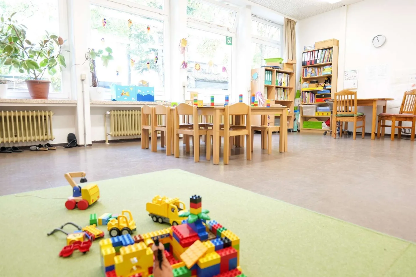 Heller Gruppenraum in der Kita Redder mit Tischgruppen und einer grünen Spielmatte, auf der Legofiguren aufgebaut sind.