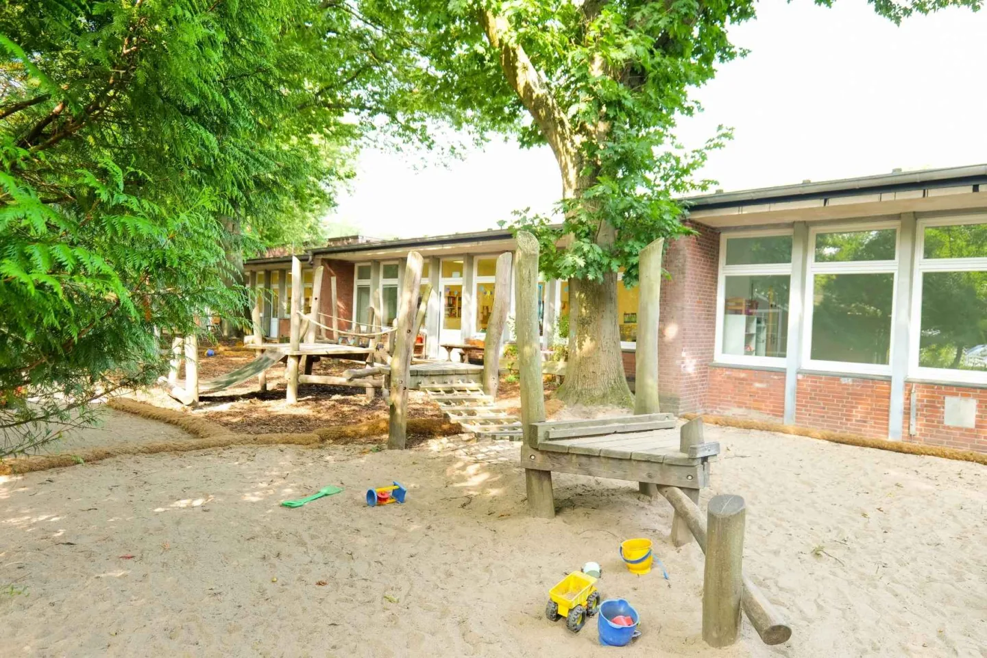 Weitläufiges, grünes Außengelände der Kita Rungwisch mit vielen Bäumen und einem Klettergerüst aus Holz.