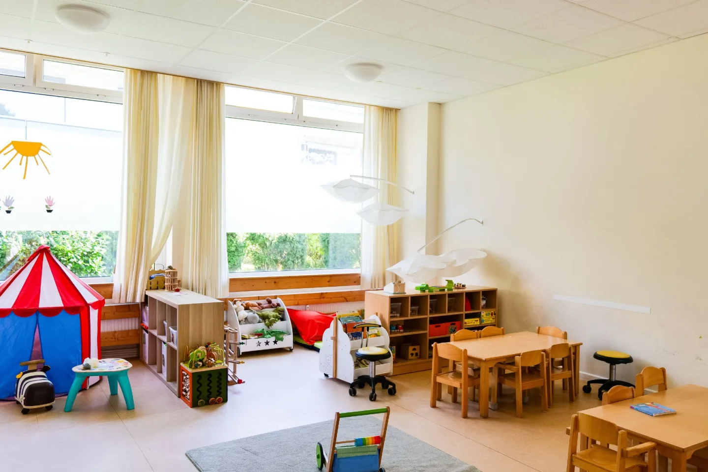 Heller, bunter Gruppenraum in der Kita Schafgarbenweg mit Tischgruppen, Spielzelt, Leseecke und vielen Spielsachen.