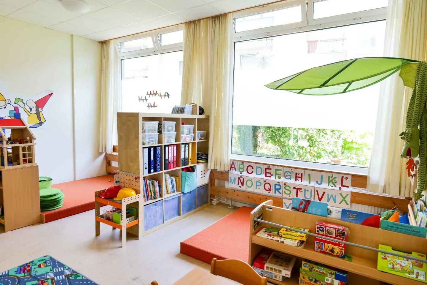 Heller, bunter Gruppenraum in der Kita Schafgarbenweg mit vielen Regalen mit Büchern, Spielzeug und gemütlichen Spiel- und Leseecken.