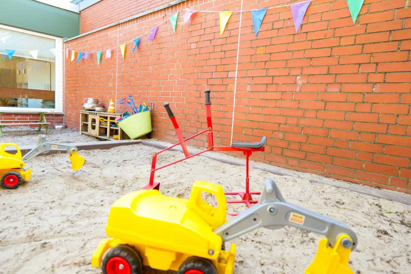 Nahaufnahme des großen Sandkastens in der Kita Schafgarbenweg mit Baggern und einer Outdoor-Spielküche.