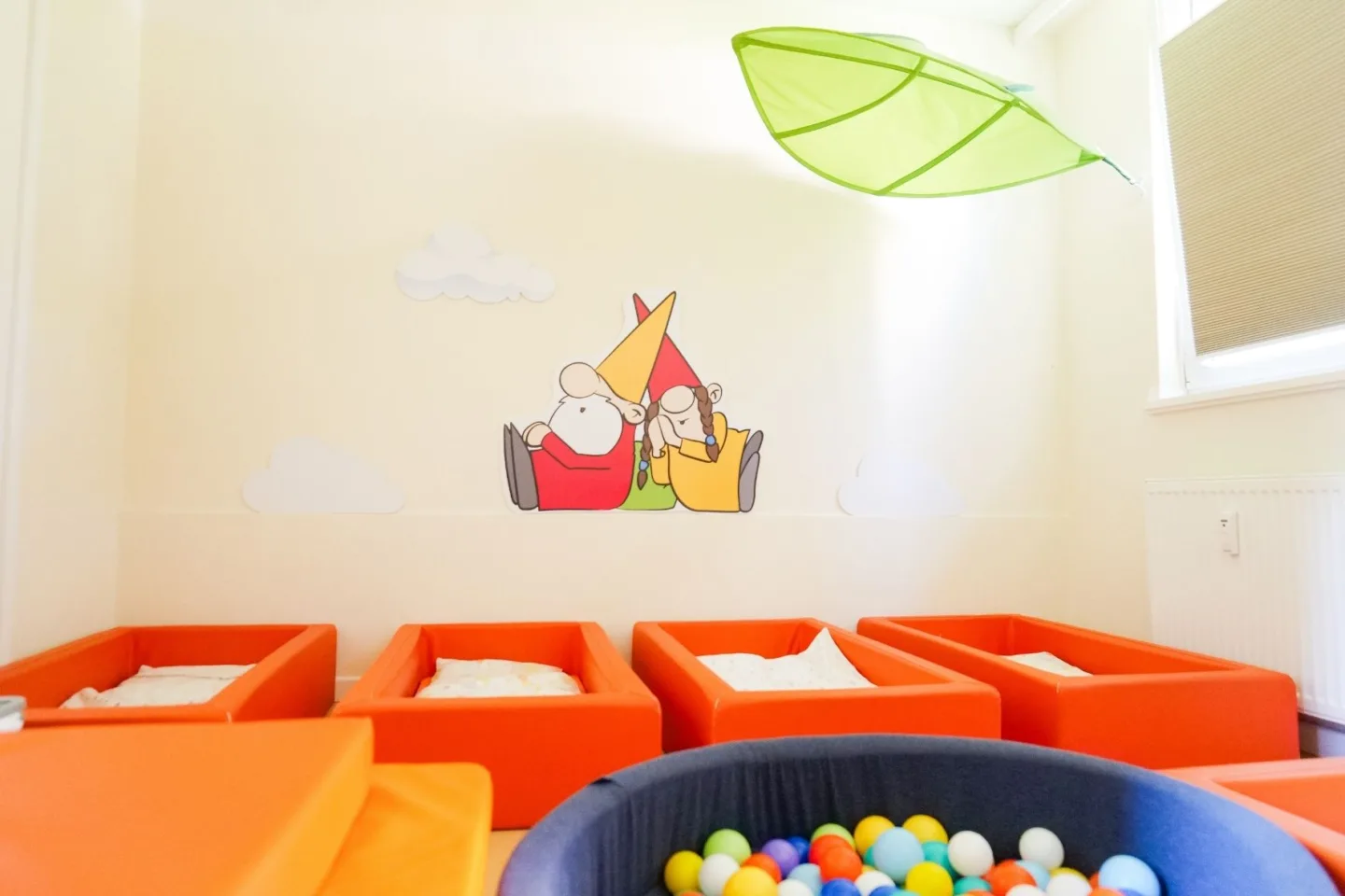 Gemütlicher Schlafbereich für Krippen-Kinder in der Kita Schafgarbenweg mit orangenen Bettchen sowie einem Bällebad.