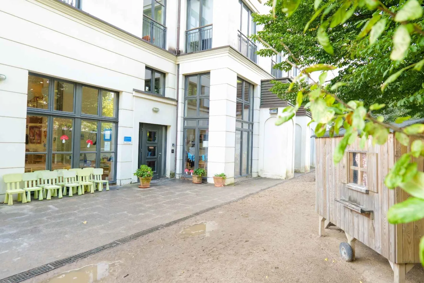 Grüner Außenbereich der Kita Völckersstraße mit einem Spielhäuschen und Kinder-Outdoor-Stühlen in der Farbe Grün.