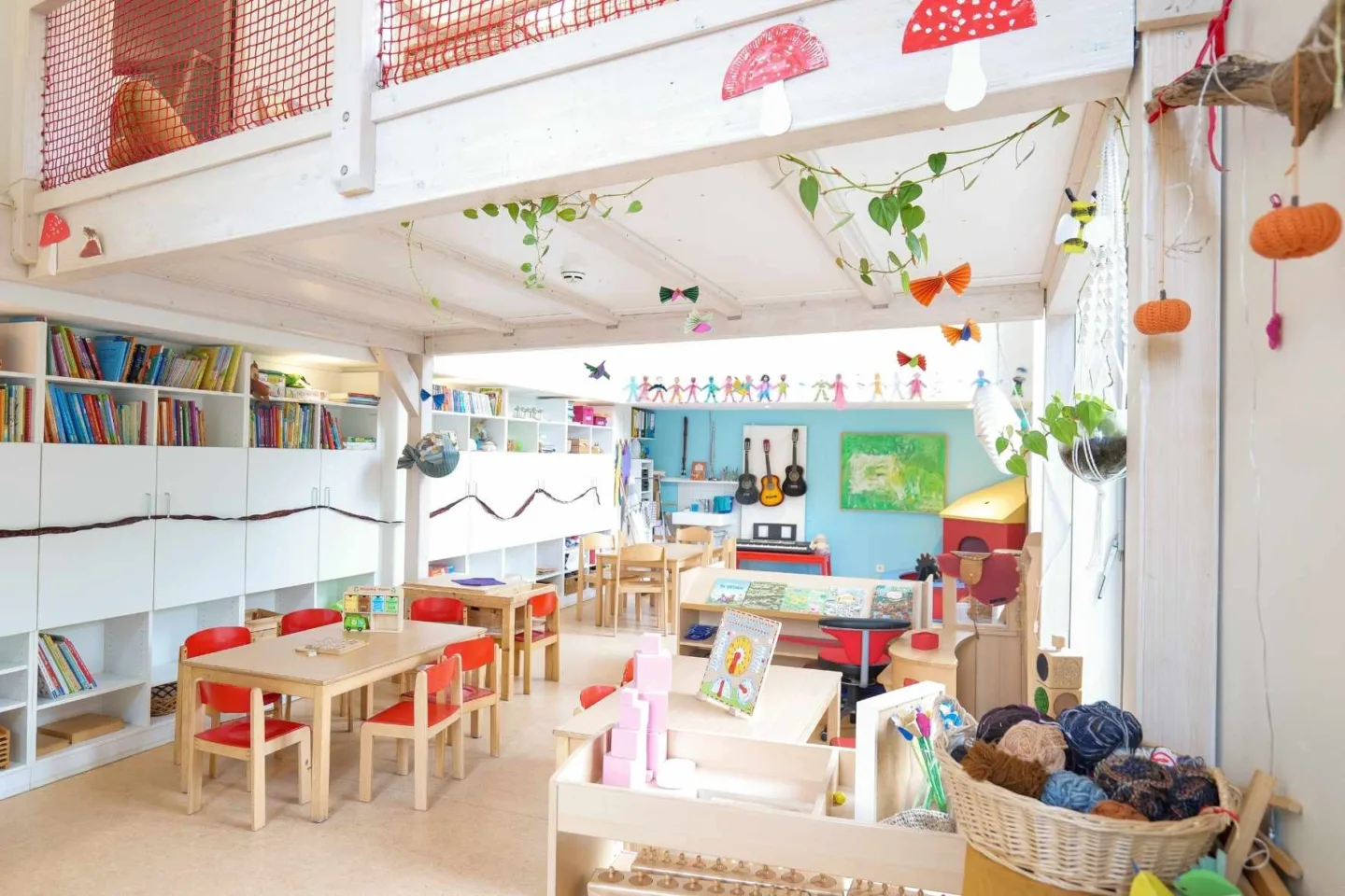 Heller, lichtdurchfluteter Gruppenraum in der Kita Völckersstraße mit Tischgruppen, Regalen mit vielen Büchern, bunter Deko an den Wänden und viel Spiel- und Bastelzeug.