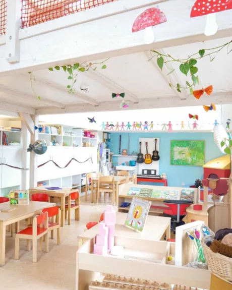 Heller, lichtdurchfluteter Gruppenraum in der Kita Völckersstraße mit Tischgruppen, Regalen mit vielen Büchern, bunter Deko an den Wänden und viel Spiel- und Bastelzeug.