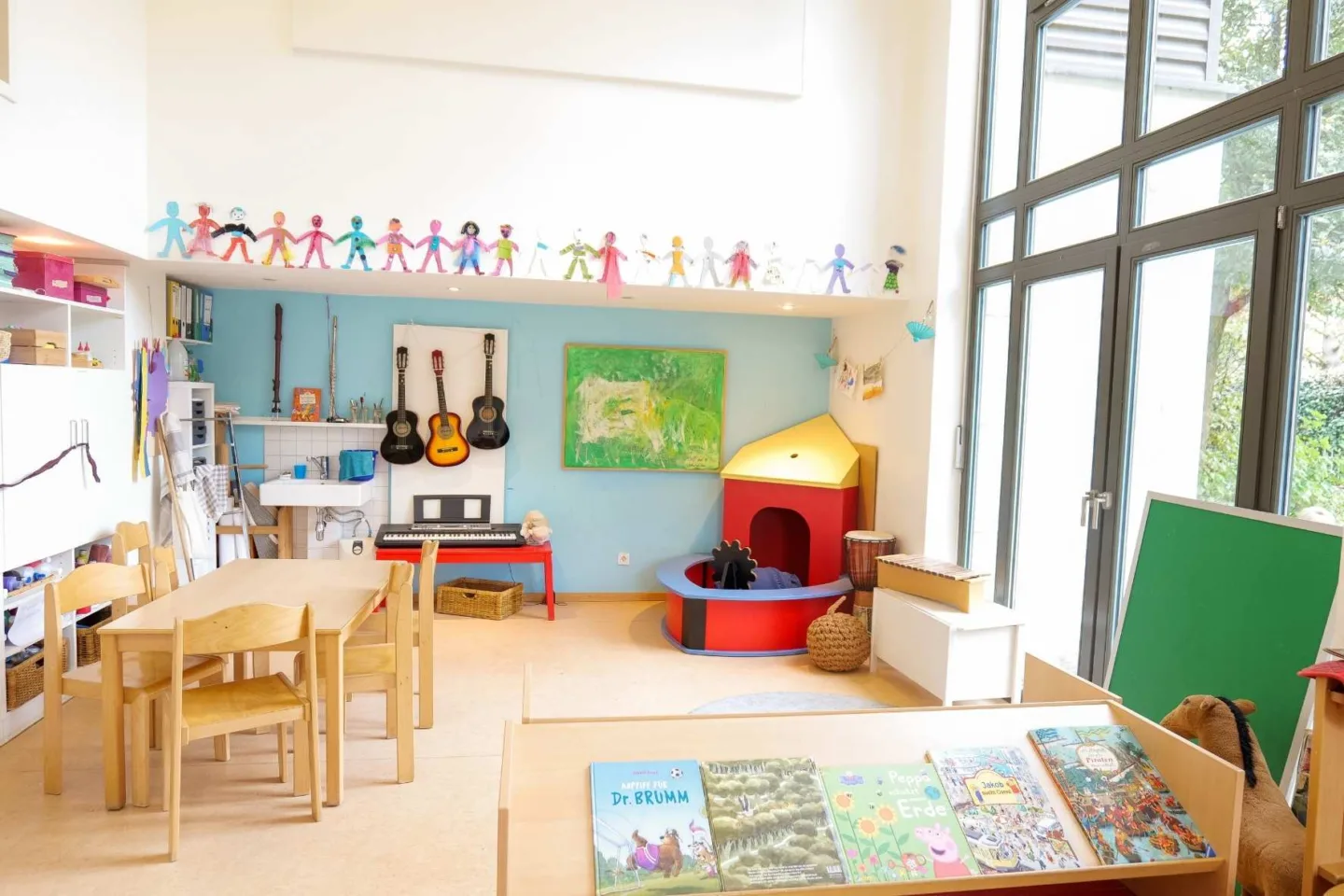 Heller, lichtdurchfluteter Gruppenraum in der Kita Völckersstraße mit einem Indoor-Spielboot, Musikinstrumenten und einer Tischgruppe.