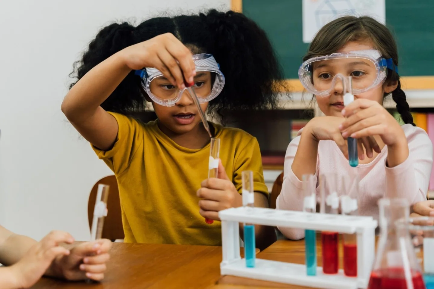 Zwei Mädchen experimentieren mit chemikalischen Flüssigkeiten und tragen dabei Schutzbrillen.